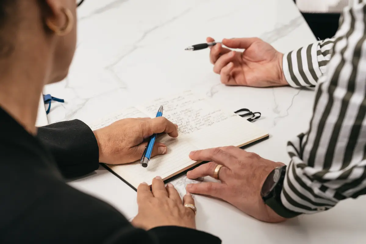 Two people working through a document together, pens and a notebook on the table