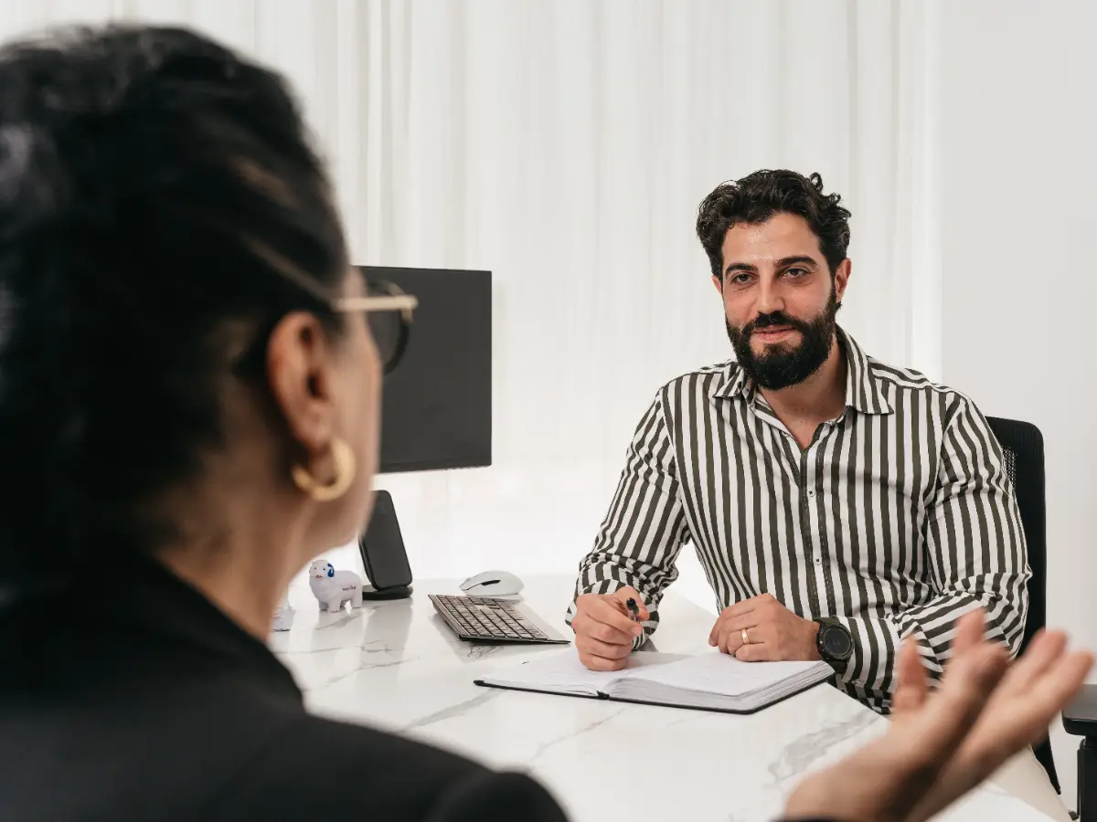 Two people in conversation across a desk, taking notes